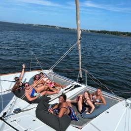 Six people relaxing on a catamaran deck, enjoying a sunny day on the water.