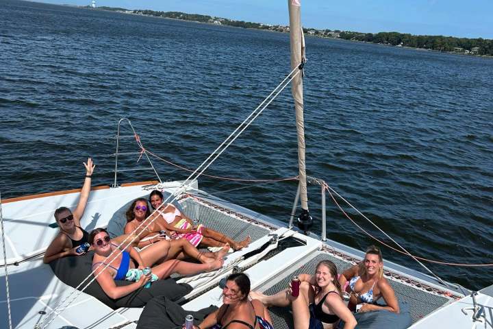 Six people relaxing on a catamaran deck, enjoying a sunny day on the water.