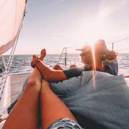 Two people lounging on a catamaran sailboat, enjoying sunny weather and ocean views.