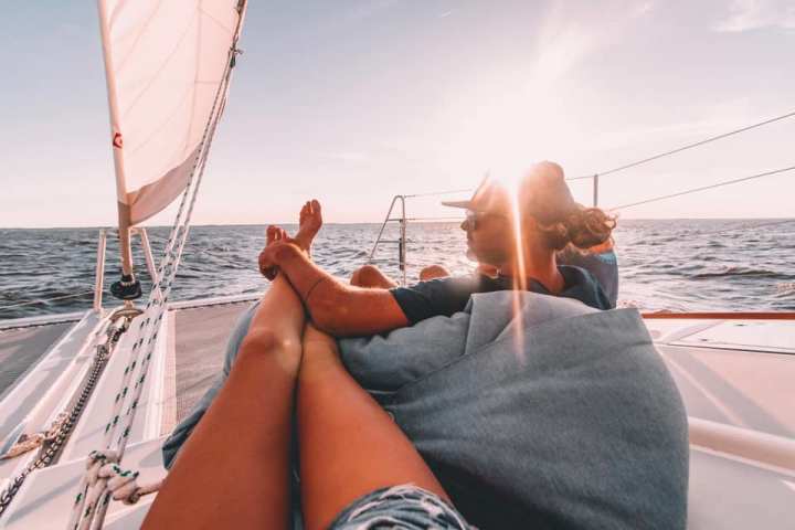 Two people lounging on a catamaran sailboat, enjoying sunny weather and ocean views.