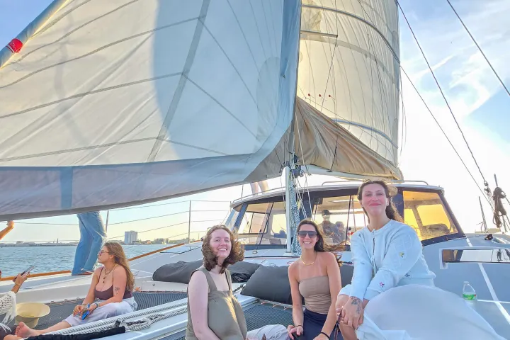 Three people sitting on a sailboat netting with large sails overhead on a sunny day.