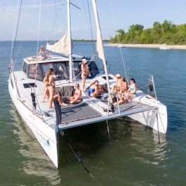 People relaxing on a catamaran sailboat on a sunny day near the shore.