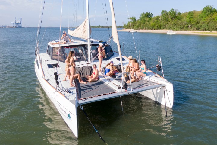 People relaxing on a catamaran sailboat on a sunny day near the shore.