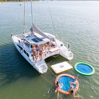 People on a catamaran enjoying water mats and a sunny day on a lake.