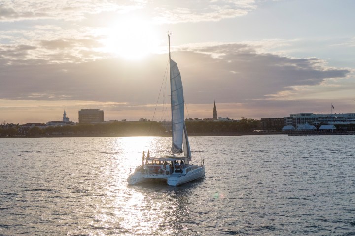 Sailboat on water with setting sun and city skyline in background.