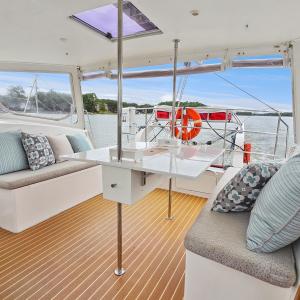 Interior of a boat with cushioned seating, pillows, and a foldable table overlooking a scenic water view.