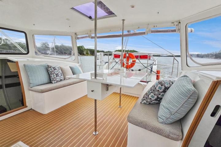 Interior of a boat with cushioned seating, pillows, and a foldable table overlooking a scenic water view.