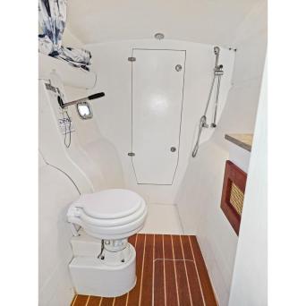 Small boat bathroom with toilet, wood floor, shower head, and door.