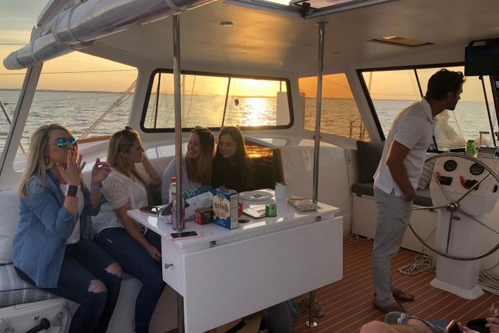 Group of people sitting on a boat at sunset, with snacks on a table.
