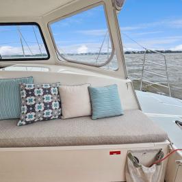 Boat interior with cushioned bench, pillows, and ocean view through windows.