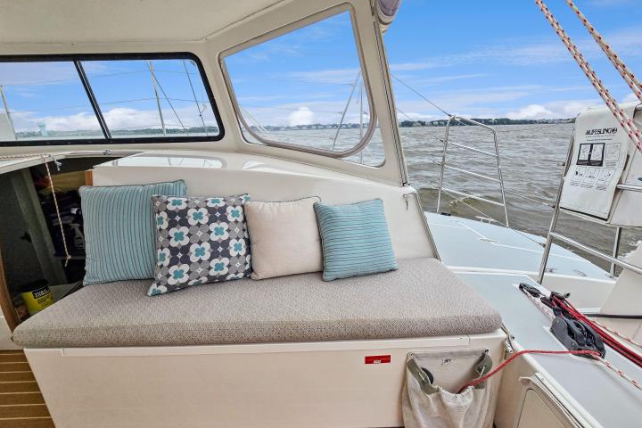 Boat interior with cushioned bench, pillows, and ocean view through windows.