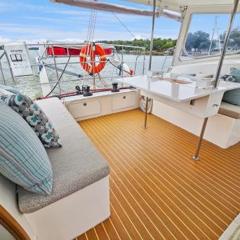 Boat interior with cushioned benches, nautical pillows, table, and view of marina through windows.