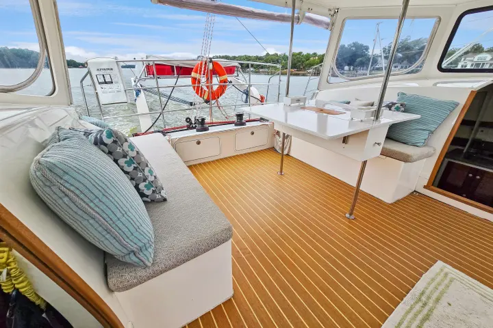 Boat interior with cushioned benches, nautical pillows, table, and view of marina through windows.