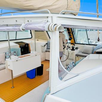 Interior view of a sailboat cockpit with cushions, table, and a person steering.