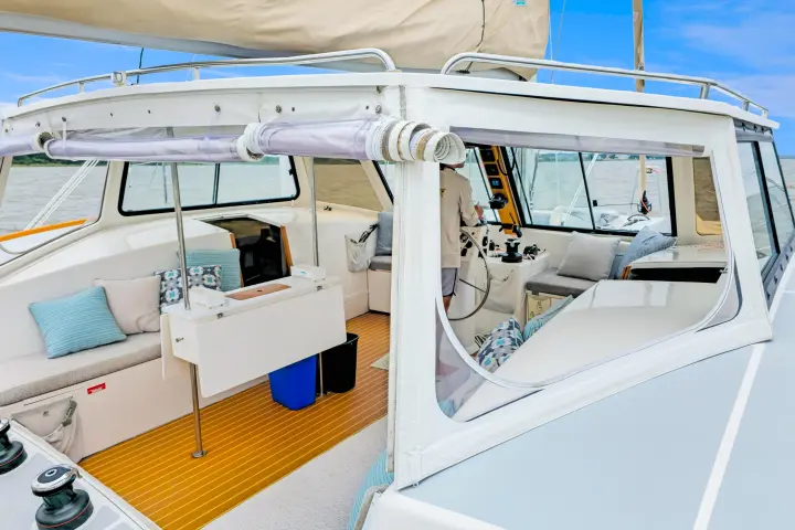 Interior view of a sailboat cockpit with cushions, table, and a person steering.