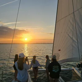 People on a sailboat watch the sunset over the ocean.