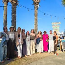 Group of people posing by palm trees near a waterfront on a sunny day.