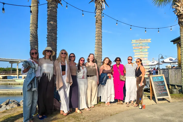 Group of people posing by palm trees near a waterfront on a sunny day.