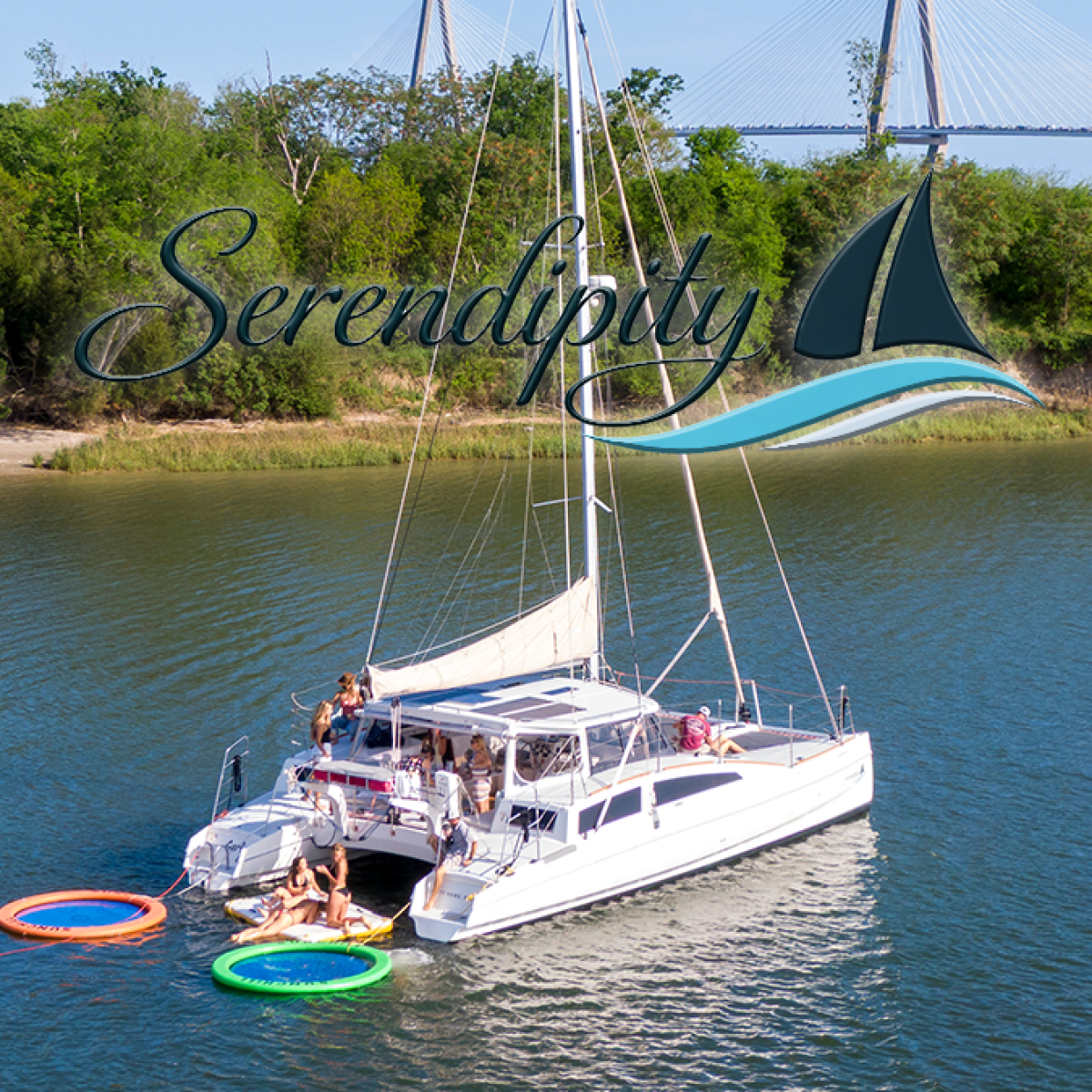 A catamaran on a river with people and inflatable rings, trees in background.